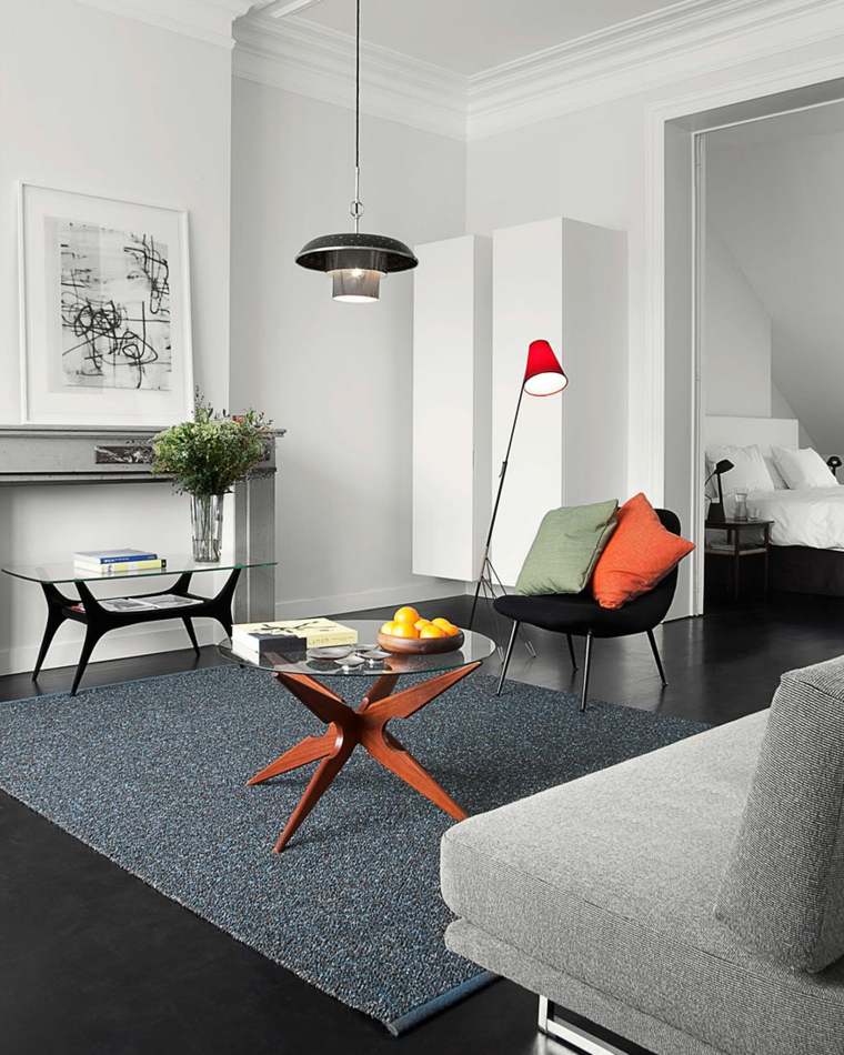 déco studio idée cadre tableau abstrait table basse verre bois tapis de sol gris foncé luminaire en suspension fauteuil noir coussin orange 