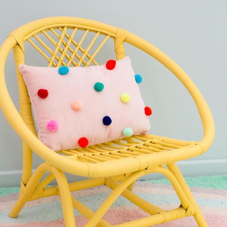 coussin rose avec des pompons sur une chaise jaune
